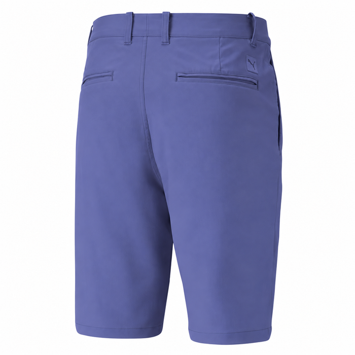 A pair of men's golf shorts in a muted periwinkle crystal blue color, shown from the back. The shorts feature belt loops, a button closure, two welt back pockets, and a small tonal embroidered logo on the upper right side.