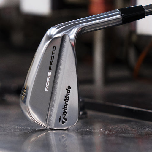 A TaylorMade RORS PROTO Golf club head on a metallic surface with a blurred background